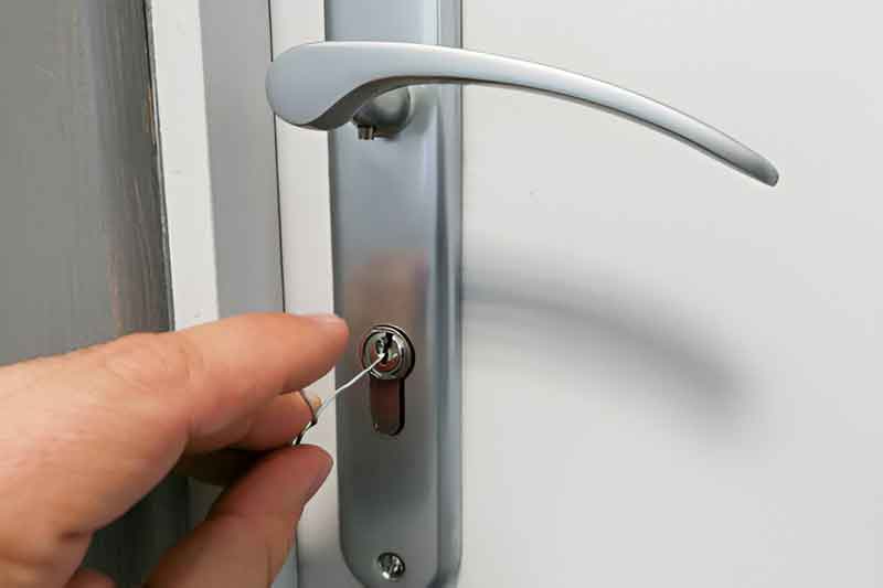 Hand picking the cylinder lock of a white uPVC door